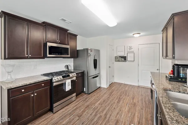a kitchen with granite countertop wooden floors stainless steel appliances and sink