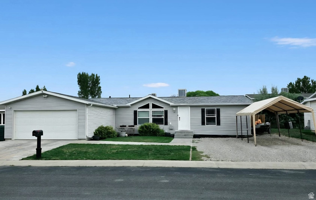 401 West 2000th Street South Vernal, UT 84078 - Photo 19 of 26 Single-story residential property featuring light gray horizontal siding, a two-car garage, front yard landscaping, a gravel driveway, and a detached carport