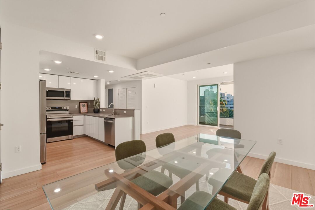 1759 North Gower Street, Unit 404 Los Angeles, CA 90028 - Photo 3 of 23 a open kitchen with stainless steel appliances kitchen island granite countertop a refrigerator a stove a sink dishwasher with a dining table and chairs