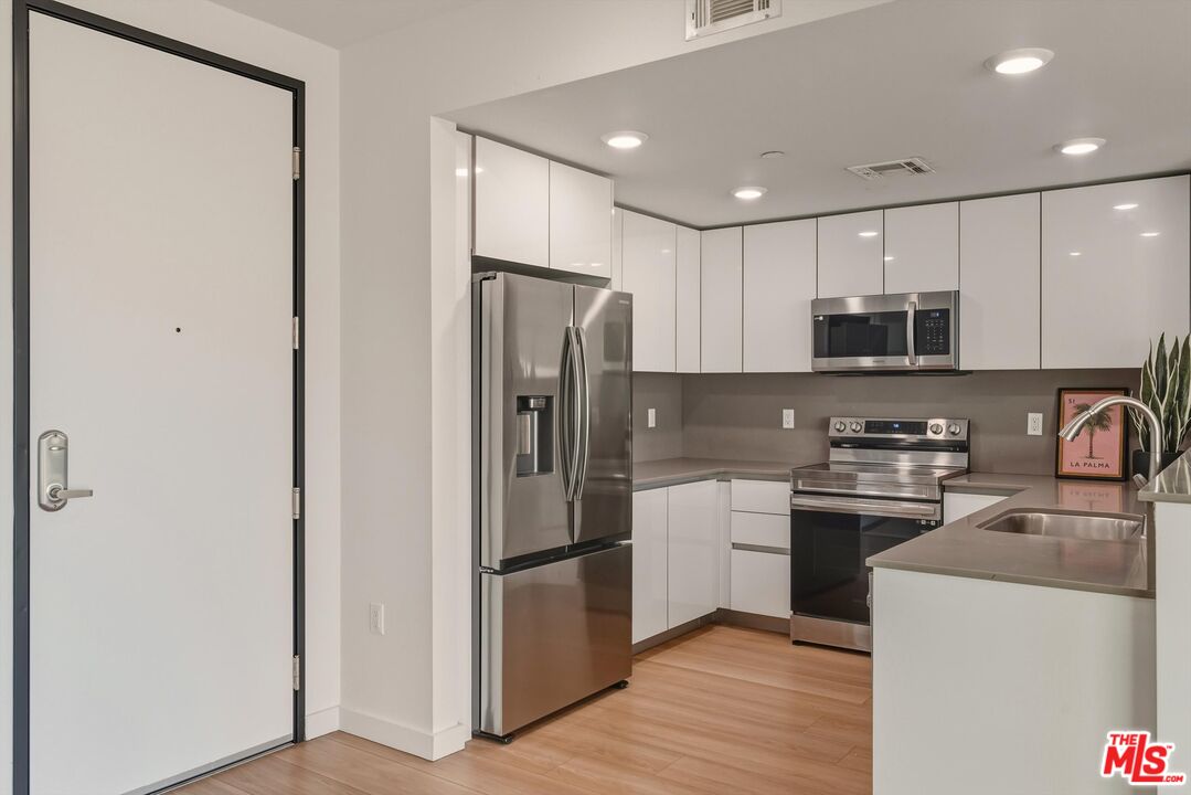 1759 North Gower Street, Unit 404 Los Angeles, CA 90028 - Photo 4 of 23 a kitchen with stainless steel appliances granite countertop a refrigerator a stove top oven a sink and dishwasher with wooden floor