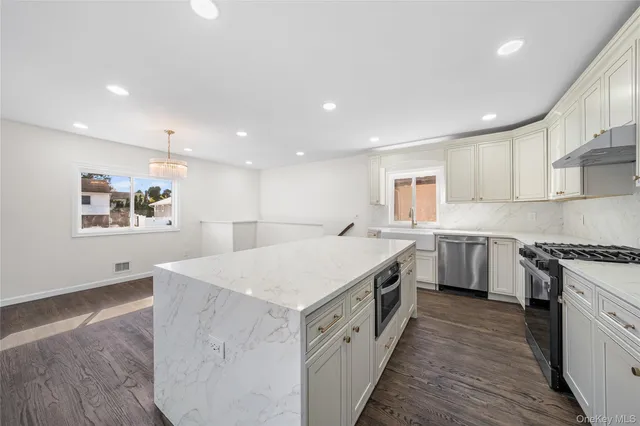 a large kitchen with stainless steel appliances granite countertop a stove a sink a refrigerator and white cabinets with wooden floor