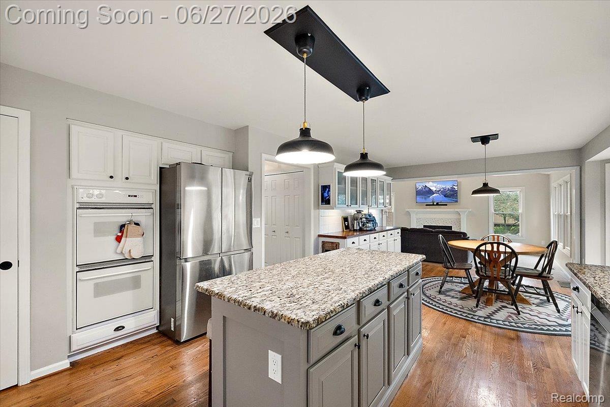 4193 Oak Tree Circle Rochester, MI 48306 - Photo 20 of 72 Open-concept kitchen featuring an island with pendant lighting, stone countertops, white cabinetry, and wood flooring