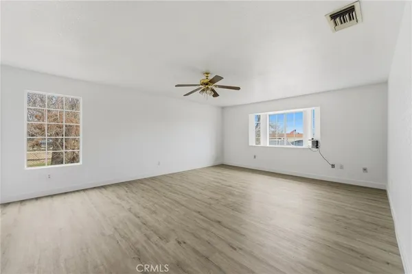an empty room with wooden floor chandelier fan and windows