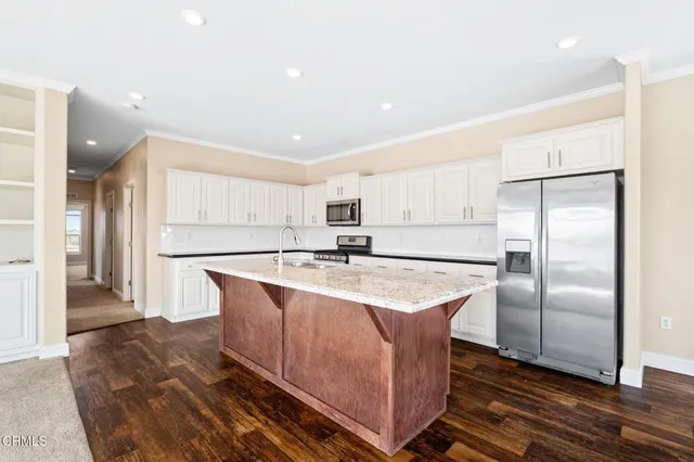a large kitchen with stainless steel appliances a sink dishwasher a refrigerator and white cabinets with wooden floor