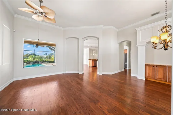 an empty room with wooden floor chandelier fan and windows