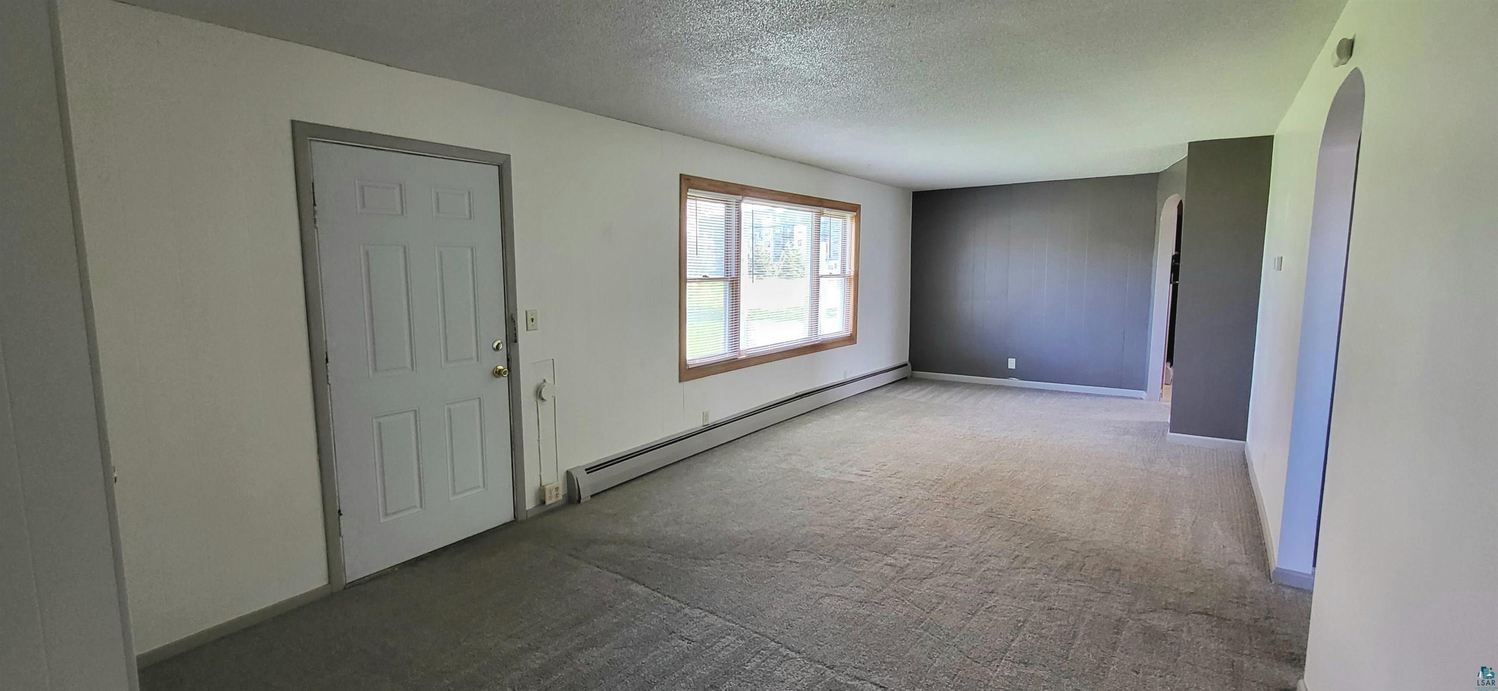 56 East 2nd Street Superior, WI 54880 - Photo 9 of 18 Spacious room featuring neutral carpet flooring, a large window with wood trim, white walls, and an arched entryway