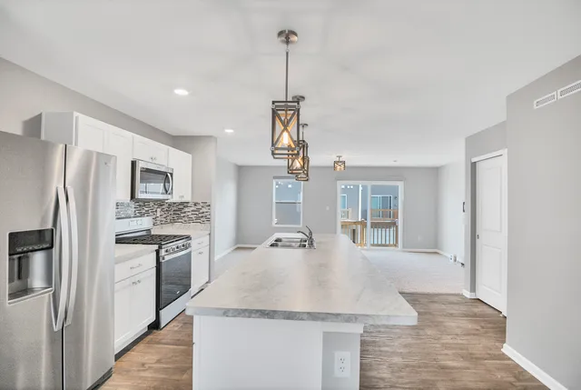 a kitchen with kitchen island granite countertop a stove top oven a sink dishwasher a refrigerator and a dining table with wooden floor