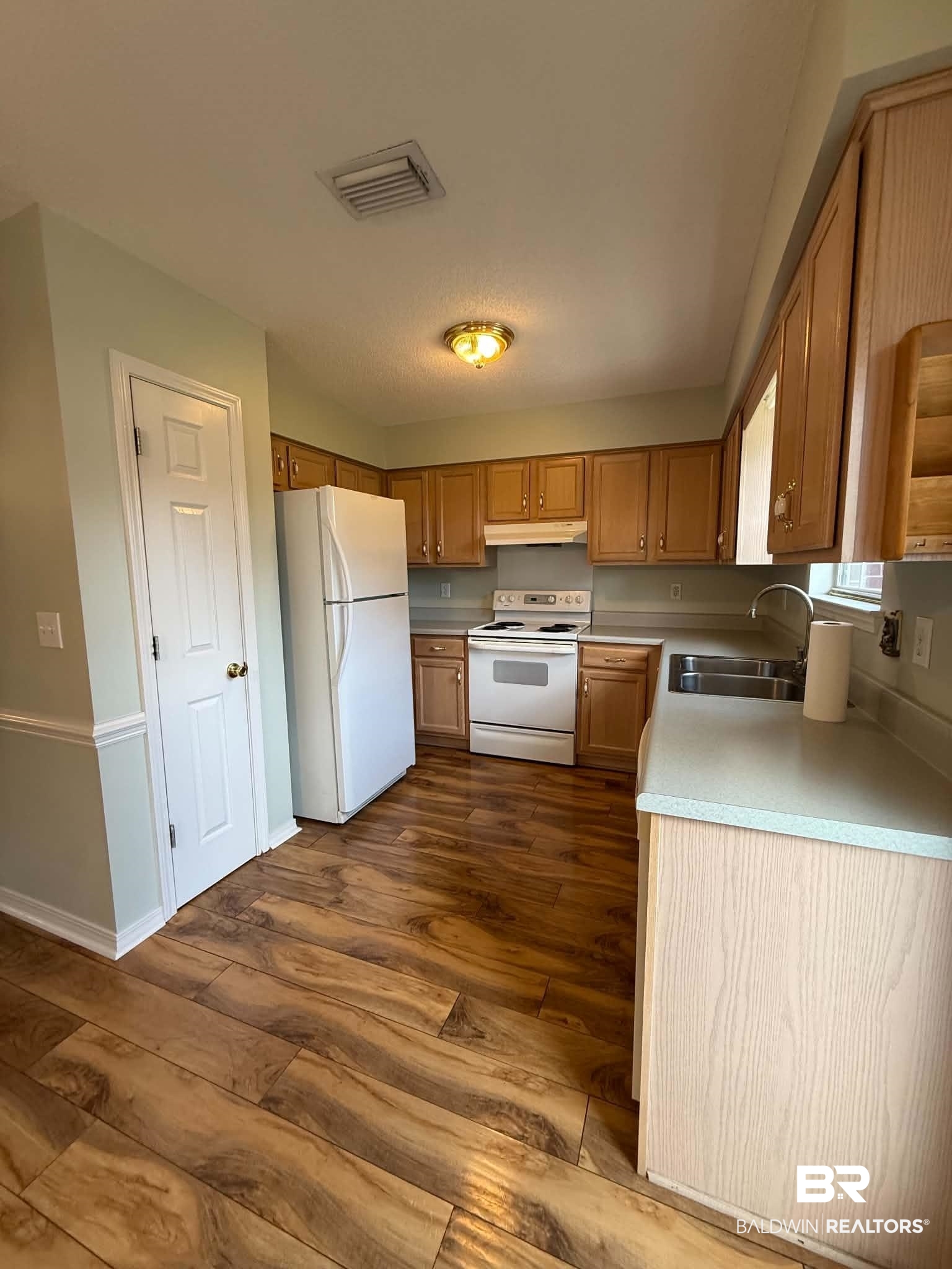 123 Pennbrooke Loop Foley, AL 36535 - Photo 28 of 49 Kitchen featuring wood-finish flooring, light wood cabinetry, light-toned countertops, a full suite of white appliances, and a double-basin stainless steel sink