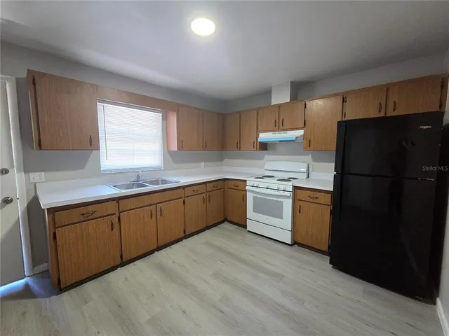 a kitchen with a refrigerator a sink wooden floor and cabinets