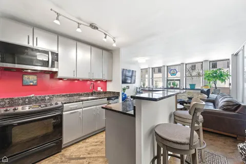 a kitchen with stainless steel appliances granite countertop a stove top oven a sink dishwasher a dining table and chairs with wooden floor