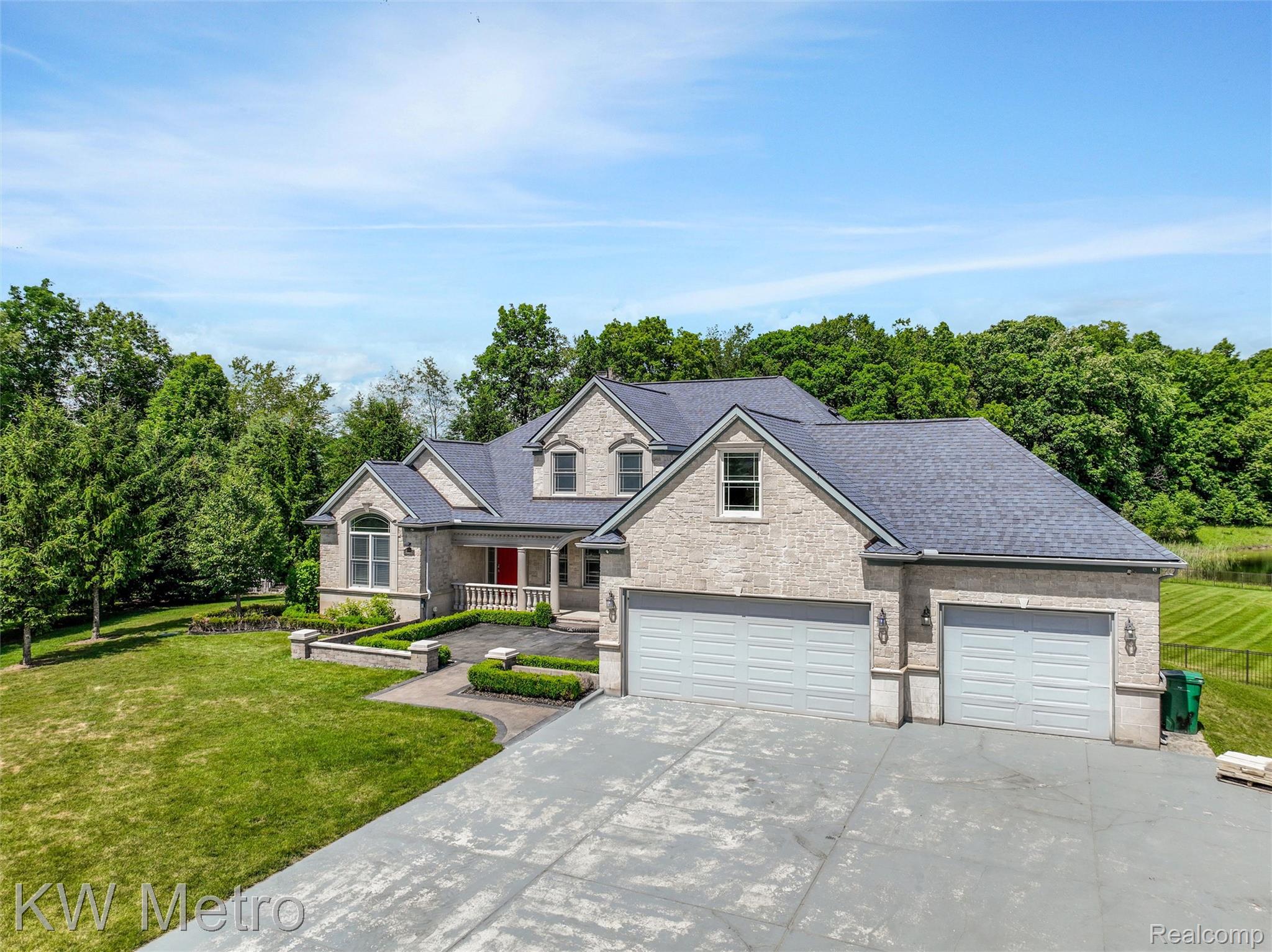65884 Windrose Court Ray, MI 48096 - Photo 4 of 82 Stone-clad residence featuring a multi-car garage, dark-shingle roofing, and a prominent red entry door