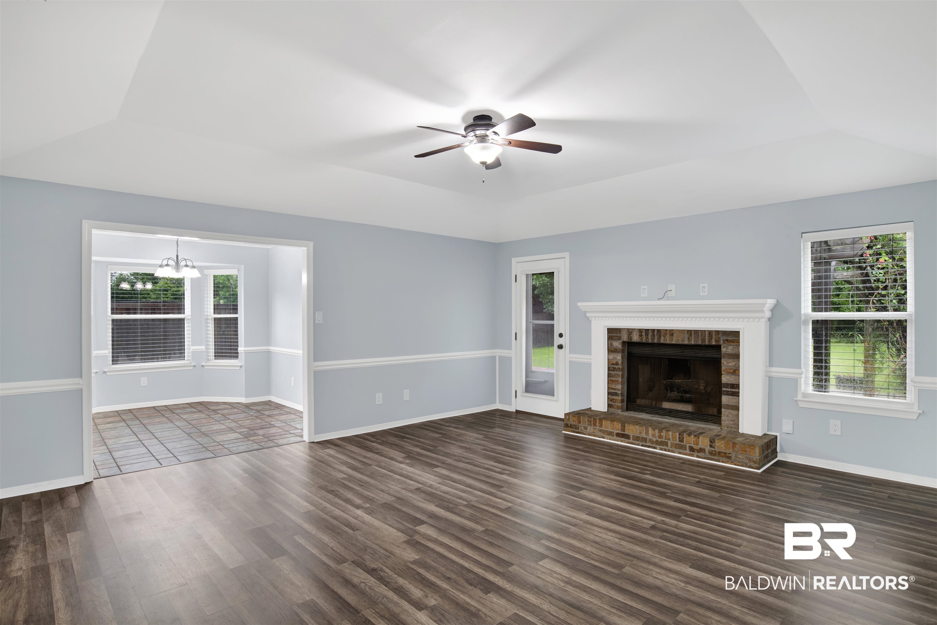 3011 Olde Gate Road Mobile, AL 36695 - Photo 8 of 35 Unfurnished living room with dark wood finished floors, ceiling fan, a chandelier, a raised ceiling, and a brick fireplace