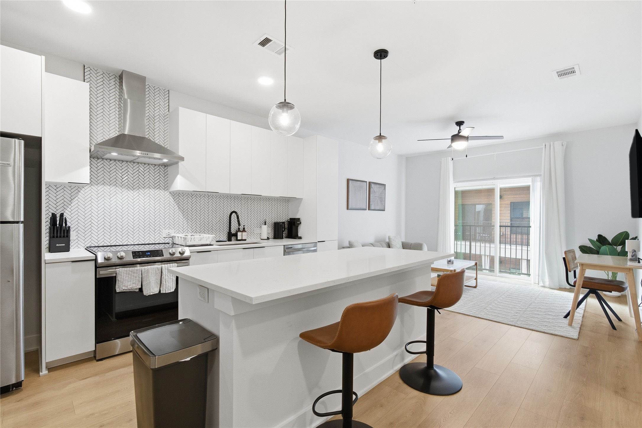 2500 Longview Street, Unit 219 Austin, TX 78705 - Photo 3 of 40 Kitchen featuring wall chimney range hood, stainless steel appliances, white cabinetry, a kitchen bar, and tasteful backsplash