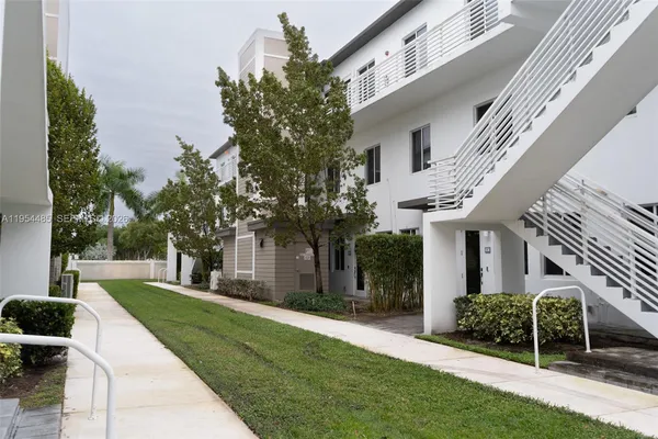 a view of a white house next to a yard with big trees