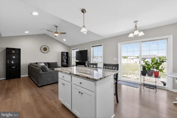 a kitchen with stainless steel appliances kitchen island granite countertop a refrigerator a stove a sink a dining table and chairs with wooden floor