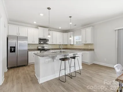 a kitchen with stainless steel appliances granite countertop a refrigerator a sink dishwasher a stove and white countertops with wooden floor