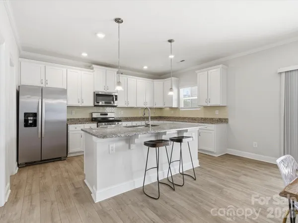 a kitchen with stainless steel appliances granite countertop a refrigerator a sink dishwasher a stove and white countertops with wooden floor
