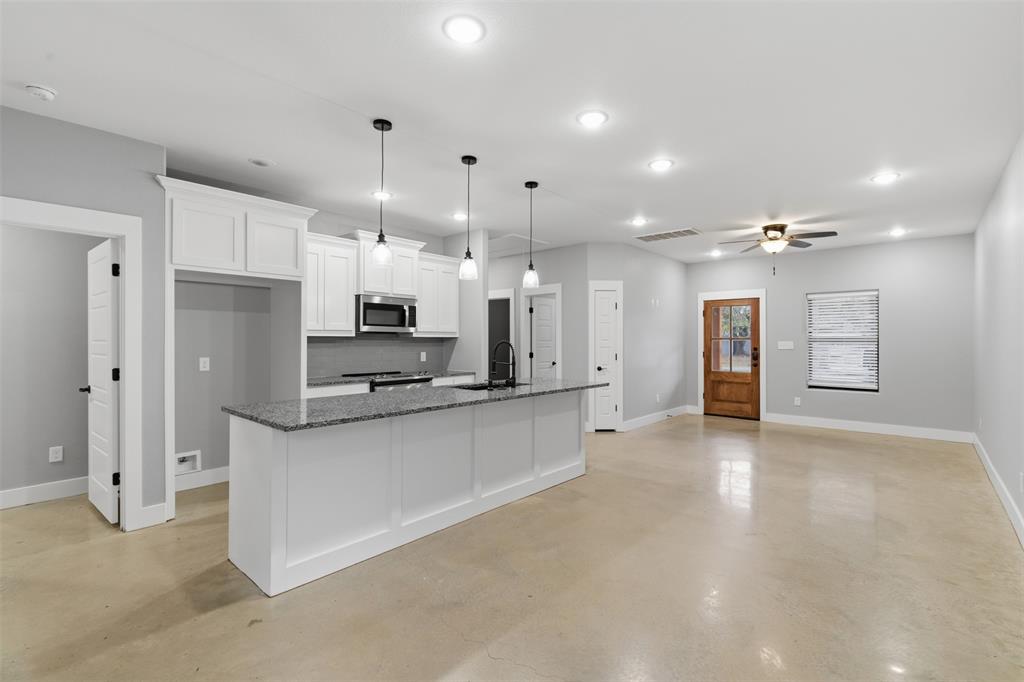 116 Harrison Street Denison, TX 75021 - Photo 6 of 25 Kitchen featuring finished concrete flooring, white cabinetry, decorative light fixtures, an island with sink, and dark stone counters