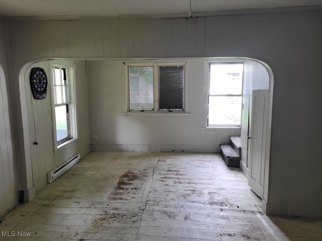 14 Ridge Street North Monroeville, OH 44847 - Photo 23 of 36 Spare room featuring a baseboard heating unit, stairs, wood walls, arched walkways, and plenty of natural light
