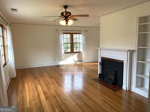 a view of an empty room with wooden floor fireplace and a window