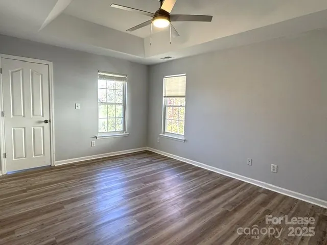 an empty room with wooden floor ceiling fan and windows