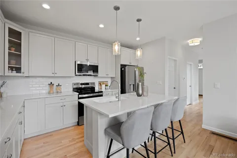 a kitchen with stainless steel appliances granite countertop a stove a sink a refrigerator a microwave oven a stove and white cabinets with wooden floor