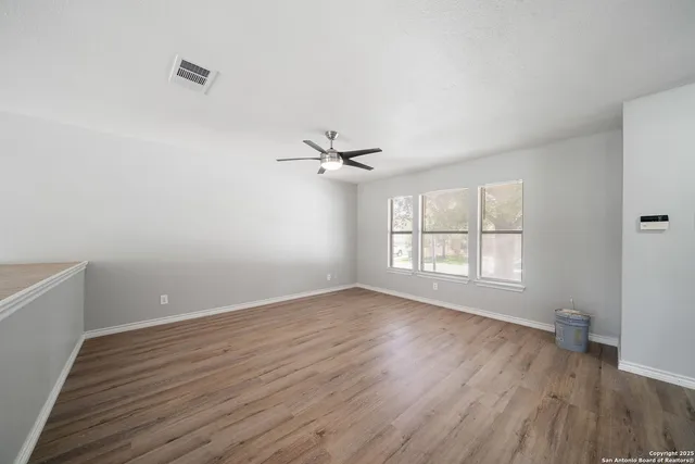 an empty room with wooden floor fan and windows