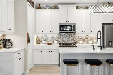 a kitchen with stainless steel appliances granite countertop a sink a stove a microwave a refrigerator and white cabinets