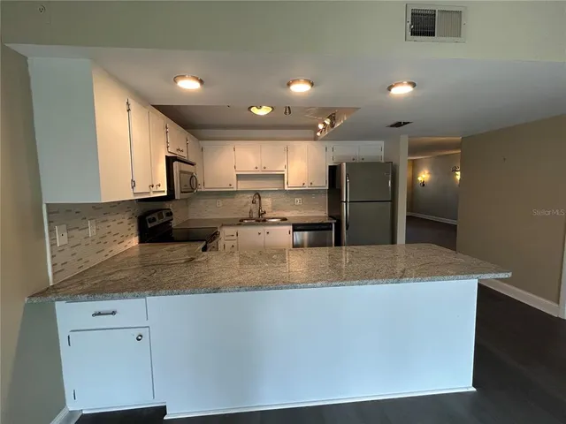 a large kitchen with granite countertop a stove a sink a refrigerator a microwave oven with white cabinets