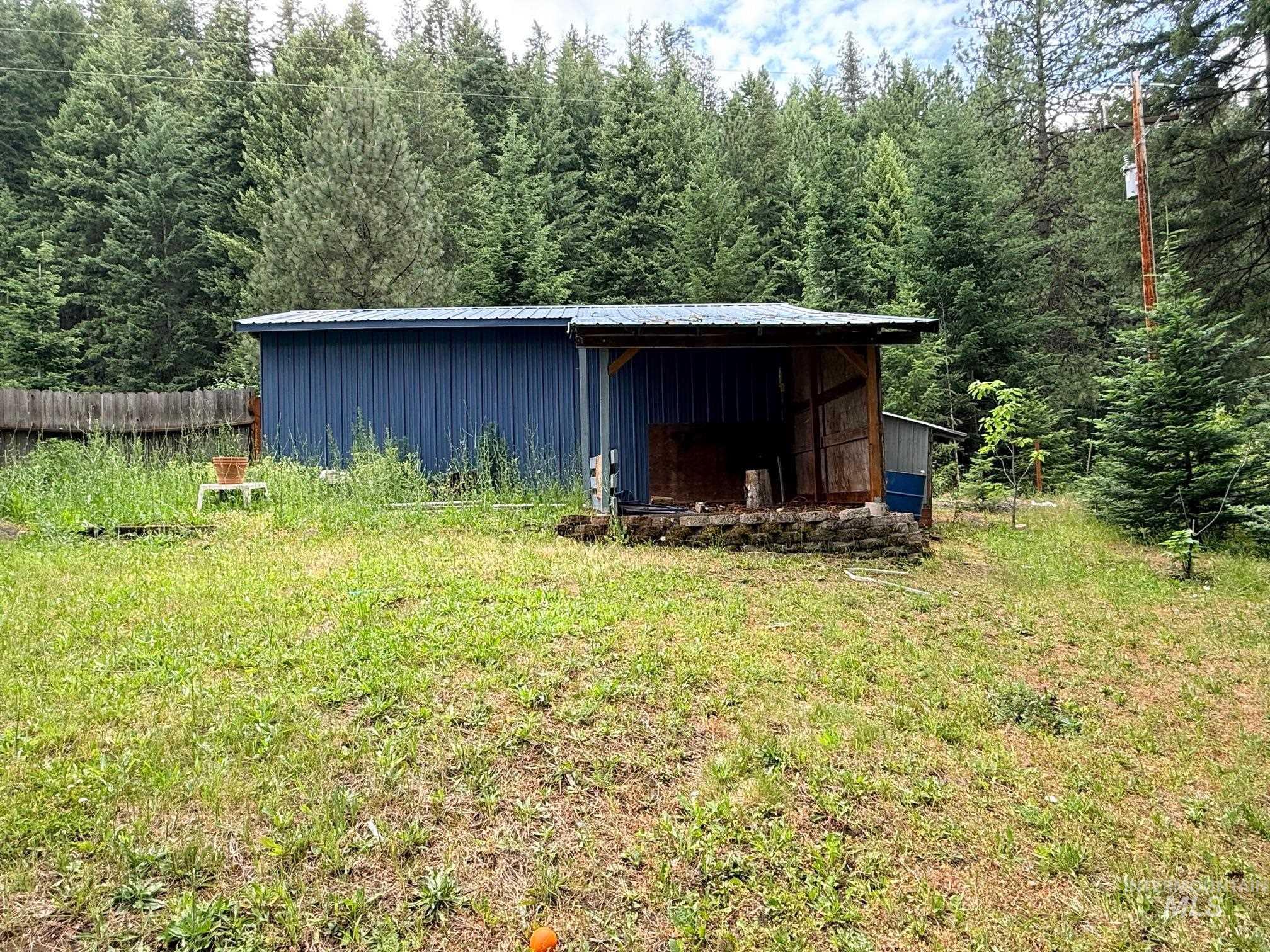 5742 Grangemont Road Orofino, ID 83544 - Photo 20 of 25 Blue metal outbuilding with an attached open-air wood structure, featuring a metal roof and a stone base