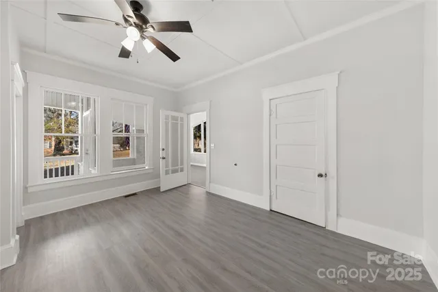 an empty room with wooden floor chandelier fan and windows