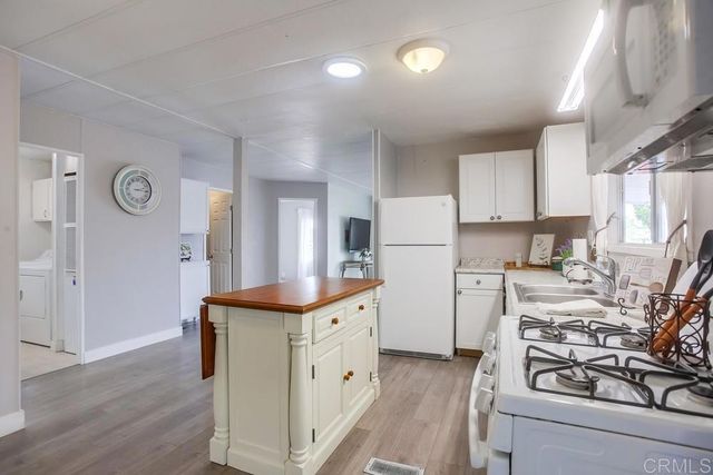 a kitchen with stainless steel appliances kitchen island granite countertop a refrigerator a stove a sink and white cabinets with wooden floor