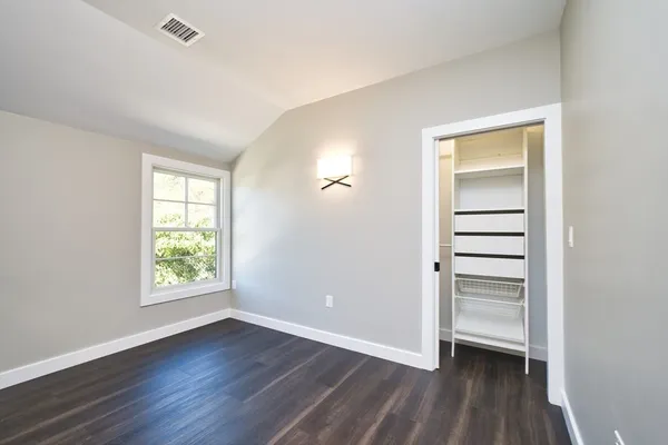 an empty room with wooden floor closet and windows