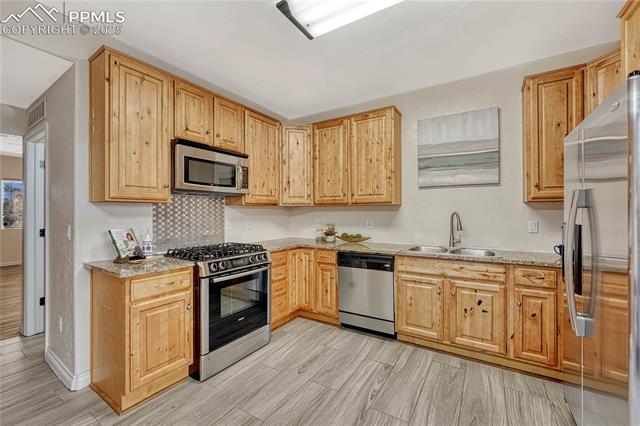 1502 York Road, Unit 102 Colorado Springs, CO 80920 - Photo 9 of 29 Kitchen featuring tasteful backsplash, light stone counters, light wood-style flooring, appliances with stainless steel finishes, and a sink