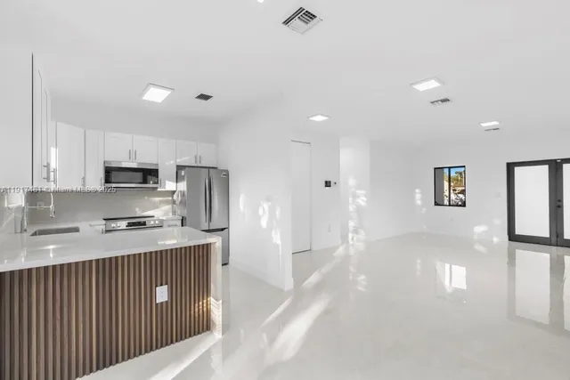 a kitchen with stainless steel appliances granite countertop a refrigerator a sink dishwasher a stove and white cabinets with wooden floor