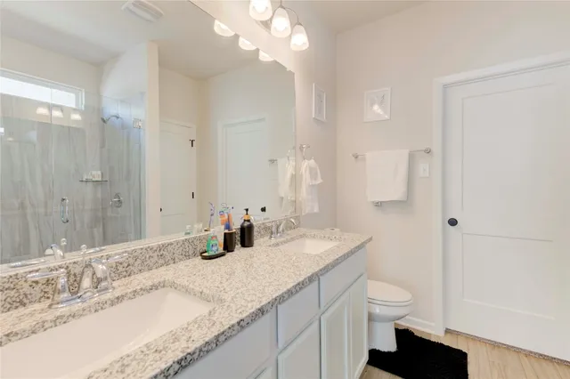 a bathroom with a granite countertop double vanity sink a mirror and a toilet