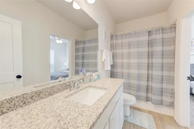 a bathroom with a granite countertop sink a toilet a mirror and shower