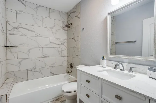 a bathroom with a granite countertop bathtub shower sink vanity mirror and toilet