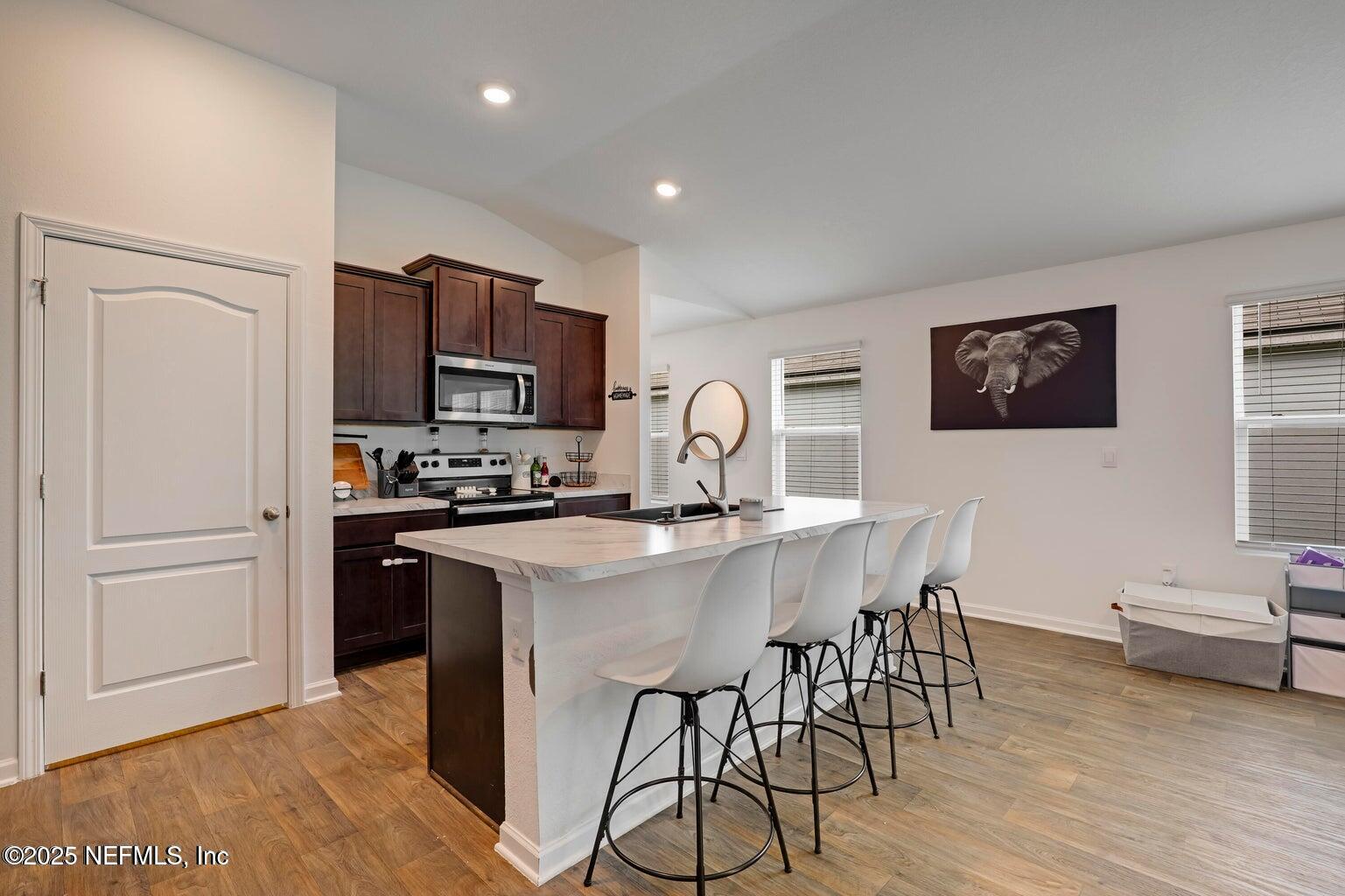 12633 Cacao Tree Trail Jacksonville, FL 32218 - Photo 19 of 44 a kitchen with stainless steel appliances granite countertop a stove a refrigerator a sink a dining table and chairs with wooden floor