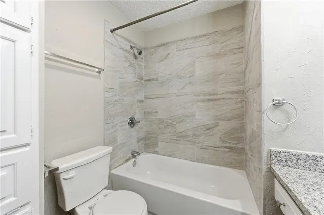 a bathroom with a granite countertop bathtub shower sink vanity and toilet