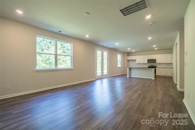 an empty room with wooden floor kitchen view and windows