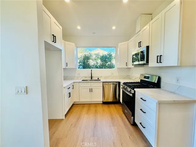 a large white kitchen with stainless steel appliances granite countertop a stove a sink and white cabinets with wooden floor