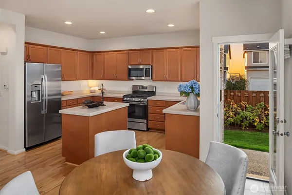 a kitchen with stainless steel appliances granite countertop a refrigerator a sink a stove a dining table and chairs