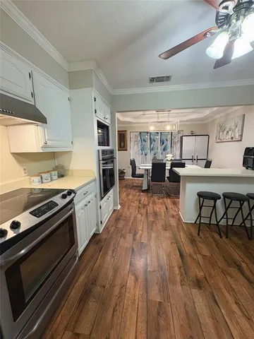 a kitchen with stainless steel appliances kitchen island granite countertop a stove top oven a sink a dining table and chairs with wooden floor