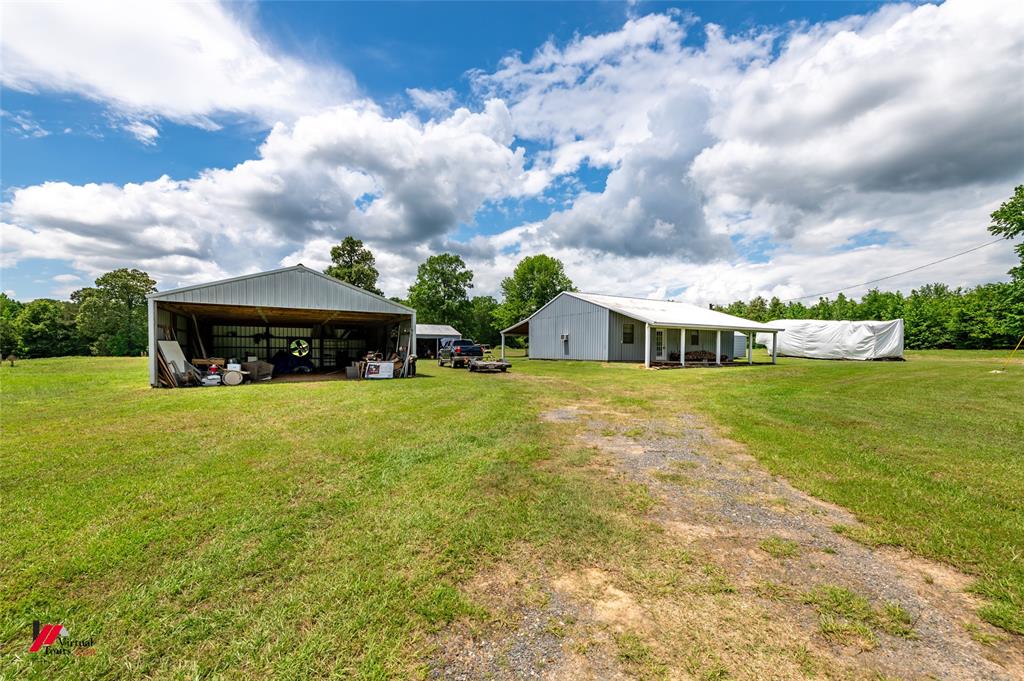 View of green lawn with a pole building, a detached carport, driveway, and an outdoor structure