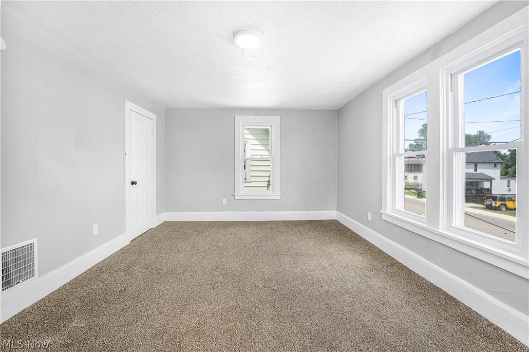 885 Wales Road Northeast Massillon, OH 44646 - Photo 15 of 34 Spacious room featuring neutral carpeting, light gray walls, white trim, multiple windows, and a flush-mount ceiling light fixture