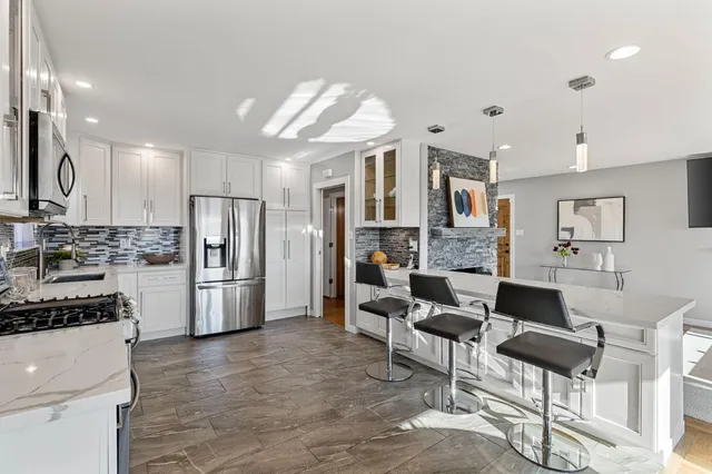 a kitchen with stainless steel appliances kitchen island granite countertop a refrigerator a stove a oven and white cabinets with wooden floor