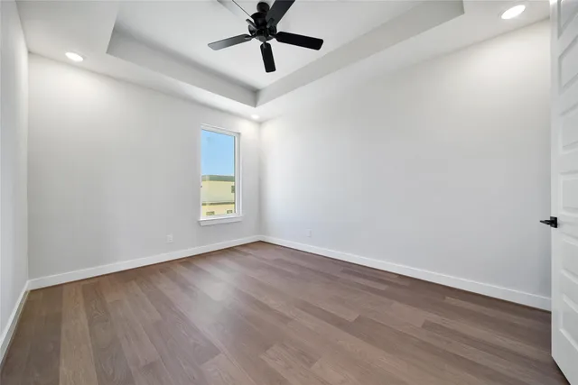 an empty room with wooden floor ceiling fan and windows