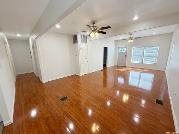 a view of an empty room with wooden floor and a ceiling fan