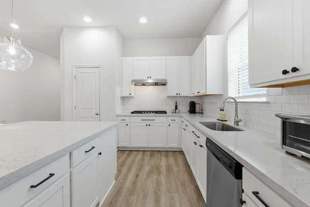 a kitchen with a sink dishwasher stove and white cabinets with wooden floor